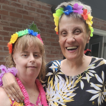 Two women with intellectual and developmental disabilities (IDD) dressed in Hawaiian costumes at a BBQ.