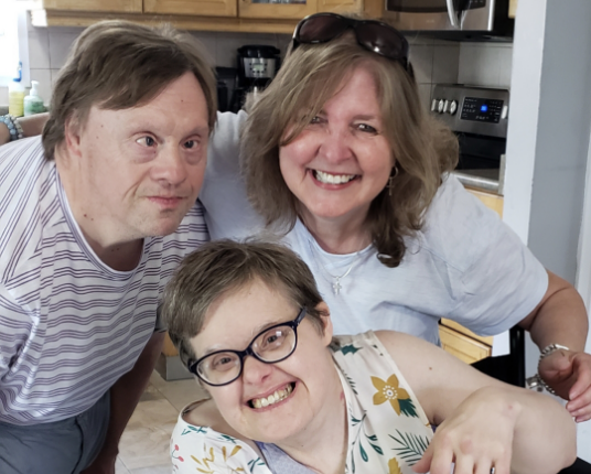 A female care worker having fun in the kitchen with two group living residents who have intellectual and developmental disabilities (IDD).